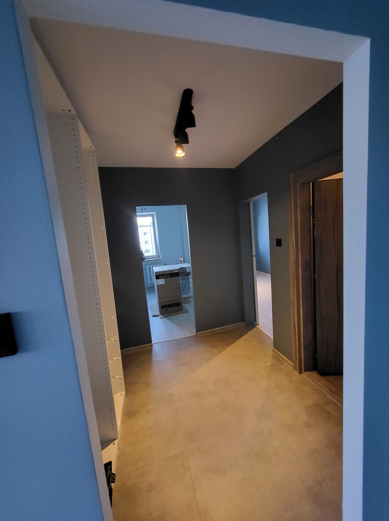 Wykończony korytarz w odcieniach szarości i beżu z zamontowanym oświetleniem punktowym i widocznymi drzwiami. W tle widoczne kartony w pokoju.