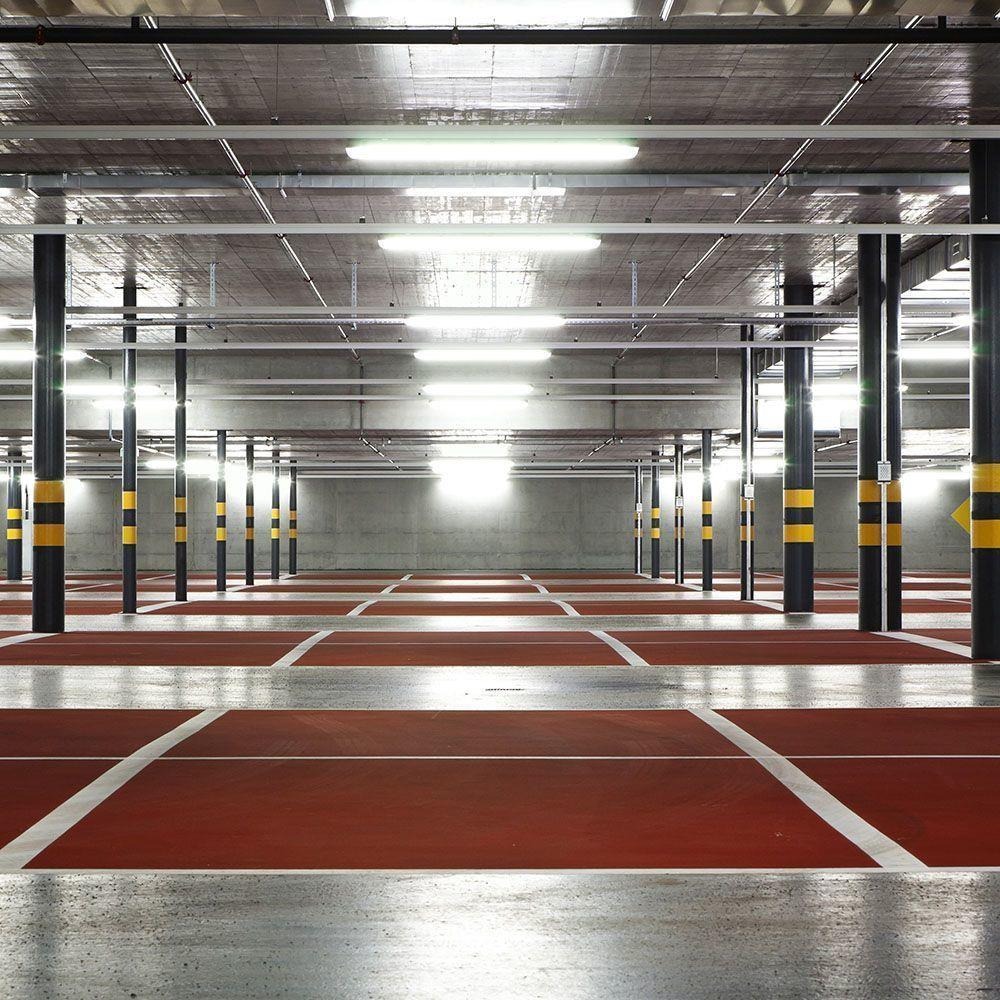 Wnętrze parkingu podziemnego z rzędami słupów w czarno-żółte pasy i rzędami fluorescencyjnych lamp pod sufitem.