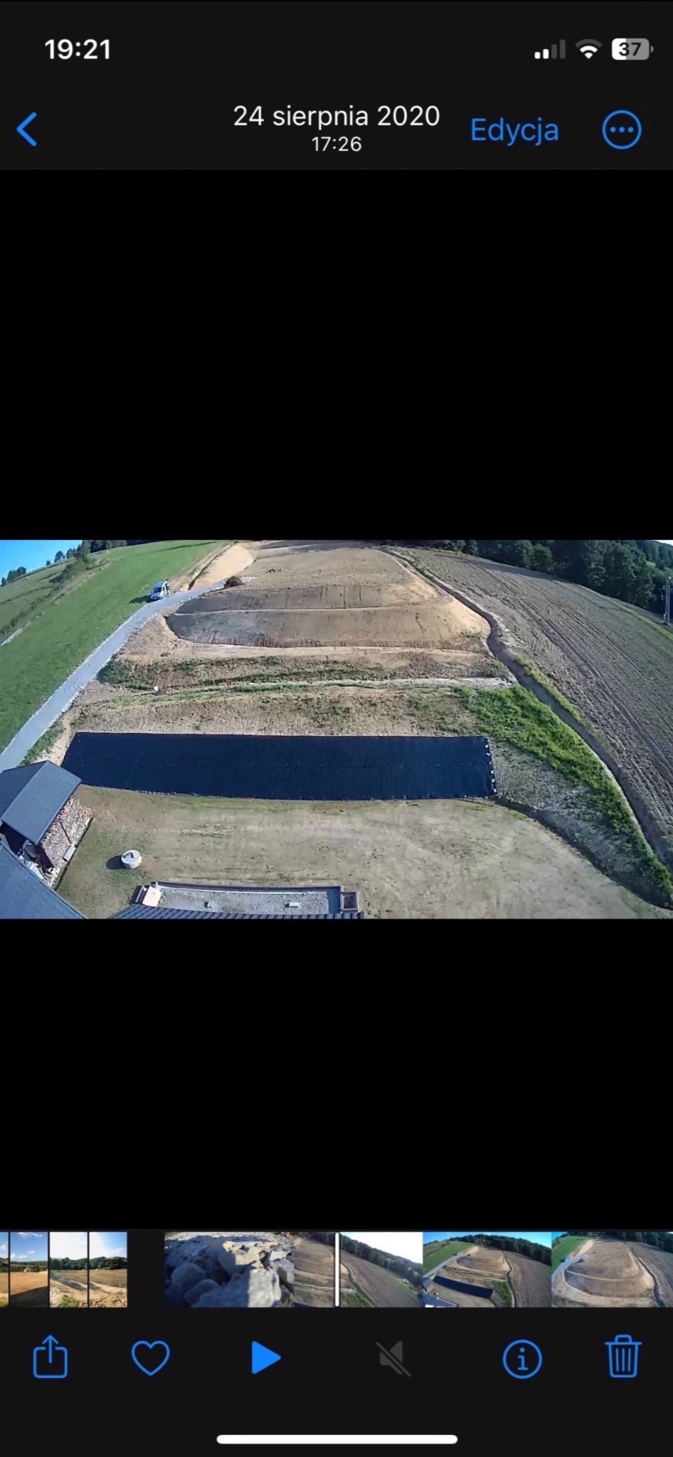 Zdjęcie z drona przedstawia przygotowany teren pod budowę domu jednorodzinnego na wzgórzu, widoczne skarpy, niwelacja terenu, droga dojazdowa oraz czarna folia zabezpieczająca.