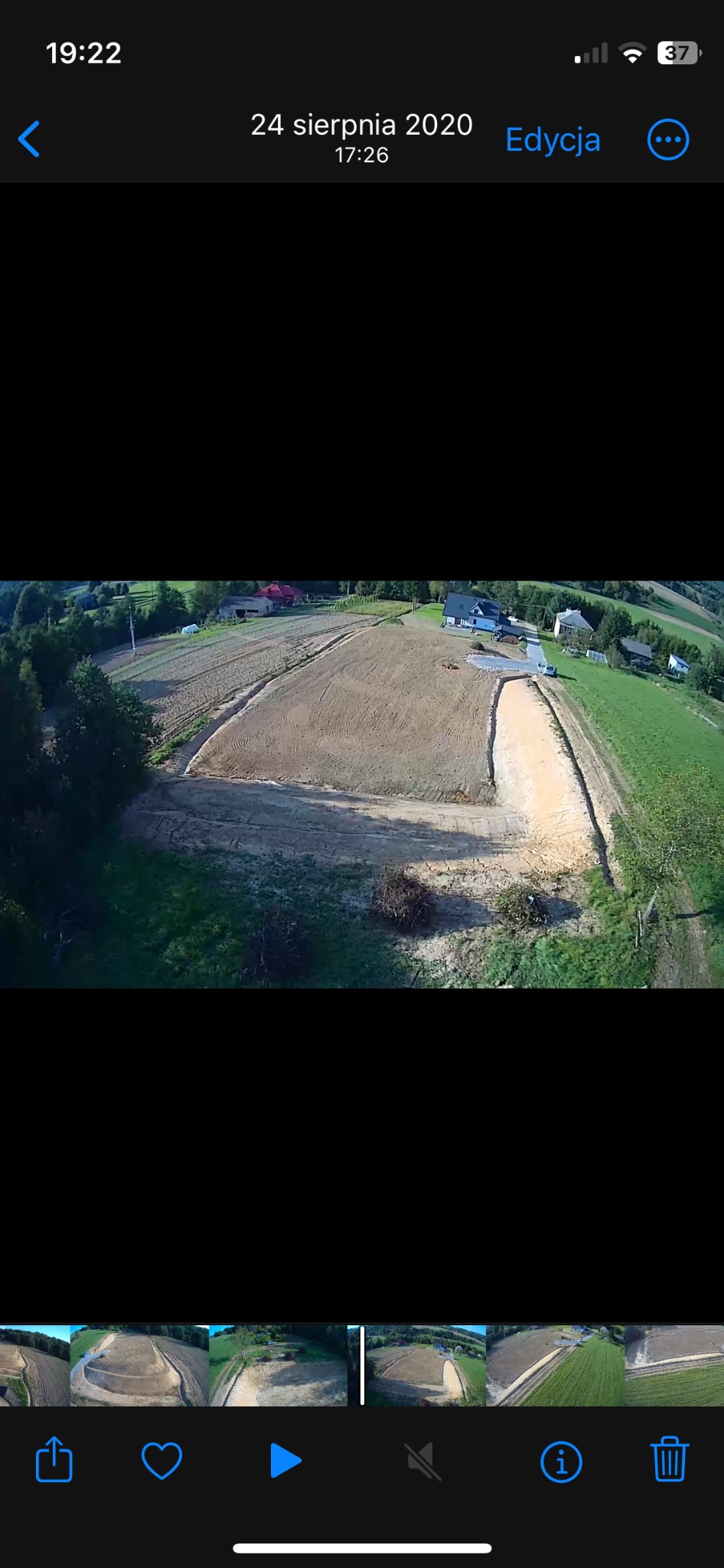 Zdjęcie z drona przedstawia wyrównany teren pod budowę domu jednorodzinnego na wzgórzu, otoczony zielenią i zabudowaniami.