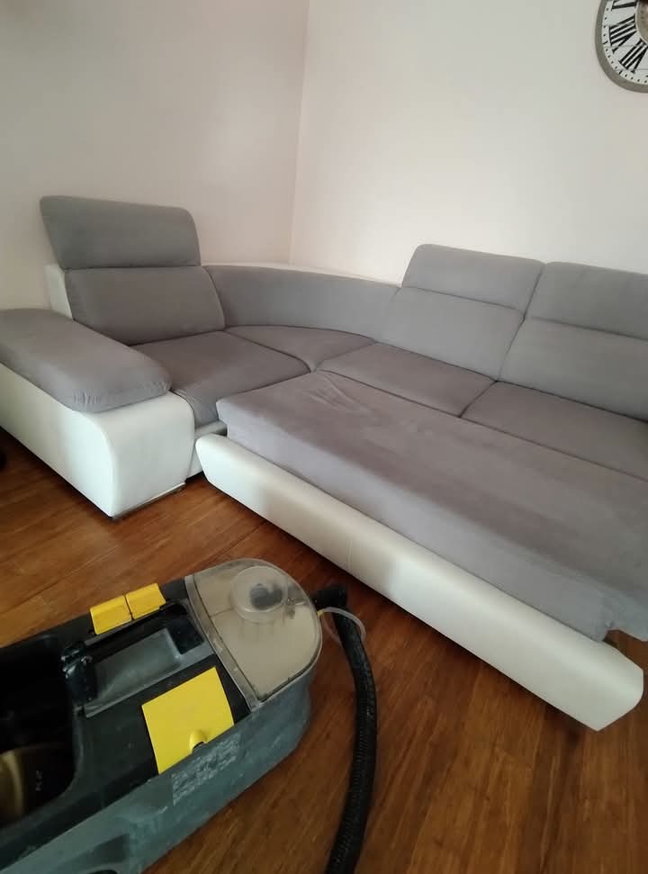 Szaro-biały narożnik po praniu, widoczny odkurzacz piorący na drewnianej podłodze. W tle zegar na ścianie.