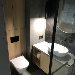 Kam-bud - Nowoczesna łazienka z umywalką nablatową, toaletą wiszącą i kabiną prysznicową z czarnymi profilami, wykończona płytkami heksagonalnymi i drewnopodobnymi panelami.