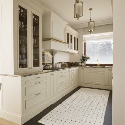 Maya Design - Elegancka kuchnia w stylu retro z kremowymi szafkami, marmurowym blatem i dekoracyjnym, wiszącym telefonem na ścianie. Na podłodze biało-czarna mozaika. Widoczne szklane witryny z zastawą.