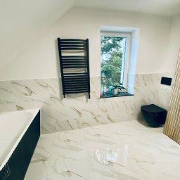 Patryk Machaj - Wykończona łazienka na poddaszu z marmurowymi płytkami, czarną armaturą i grzejnikiem drabinkowym. Widok na okno z zielenią. Nowoczesny design.