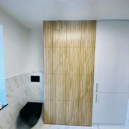 Patryk Machaj - Nowoczesna łazienka z czarną toaletą podwieszaną, marmurowymi płytkami i drewnianą ścianką z lameli. Minimalistyczne oświetlenie sufitowe.