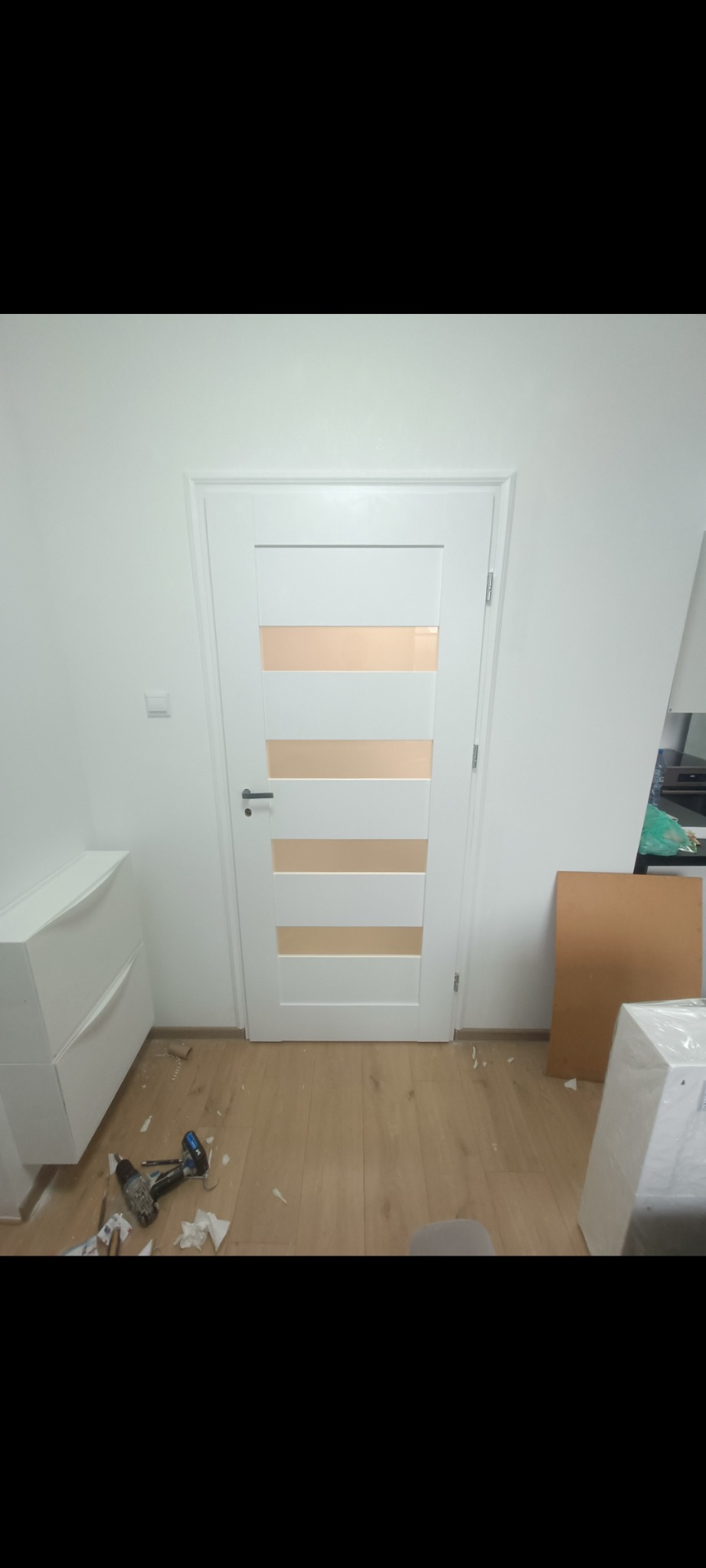 Białe drzwi wewnętrzne z poziomymi, matowymi przeszkleniami, zamontowane w białej ścianie. Na podłodze widoczne narzędzia i resztki po montażu.