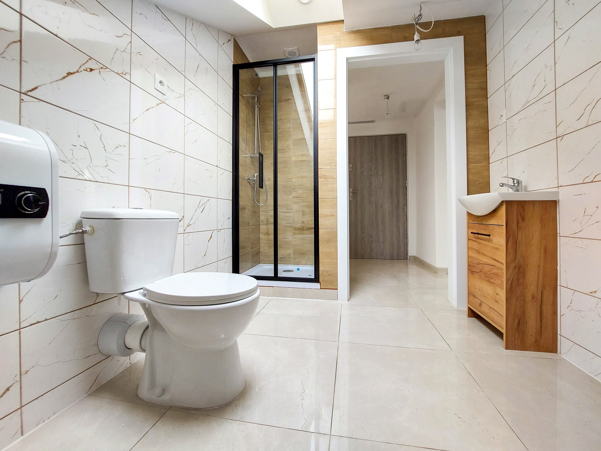 Nowoczesna łazienka z kabiną prysznicową z czarnymi ramami, wiszącą toaletą, umywalką na szafce z drewnianym fornirem i płytkami imitującymi marmur na ścianach i podłodze.