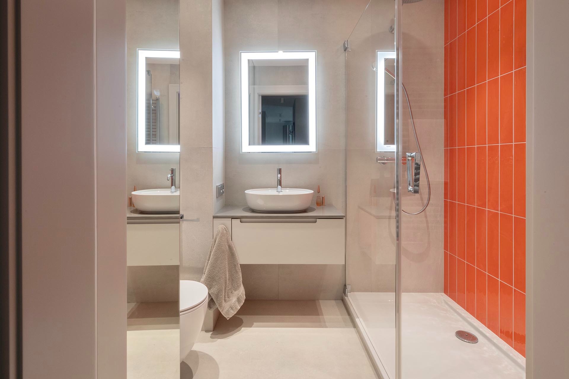 Nowoczesna łazienka w Warszawie z podświetlanymi lustrami, umywalką nablatową i kabiną prysznicową z pomarańczowymi płytkami.