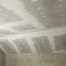 MAL-BUD - Sufit poddasza w trakcie szpachlowania, widoczne łączenia płyt gipsowo-kartonowych z nałożoną masą szpachlową, surowa ściana w tle.