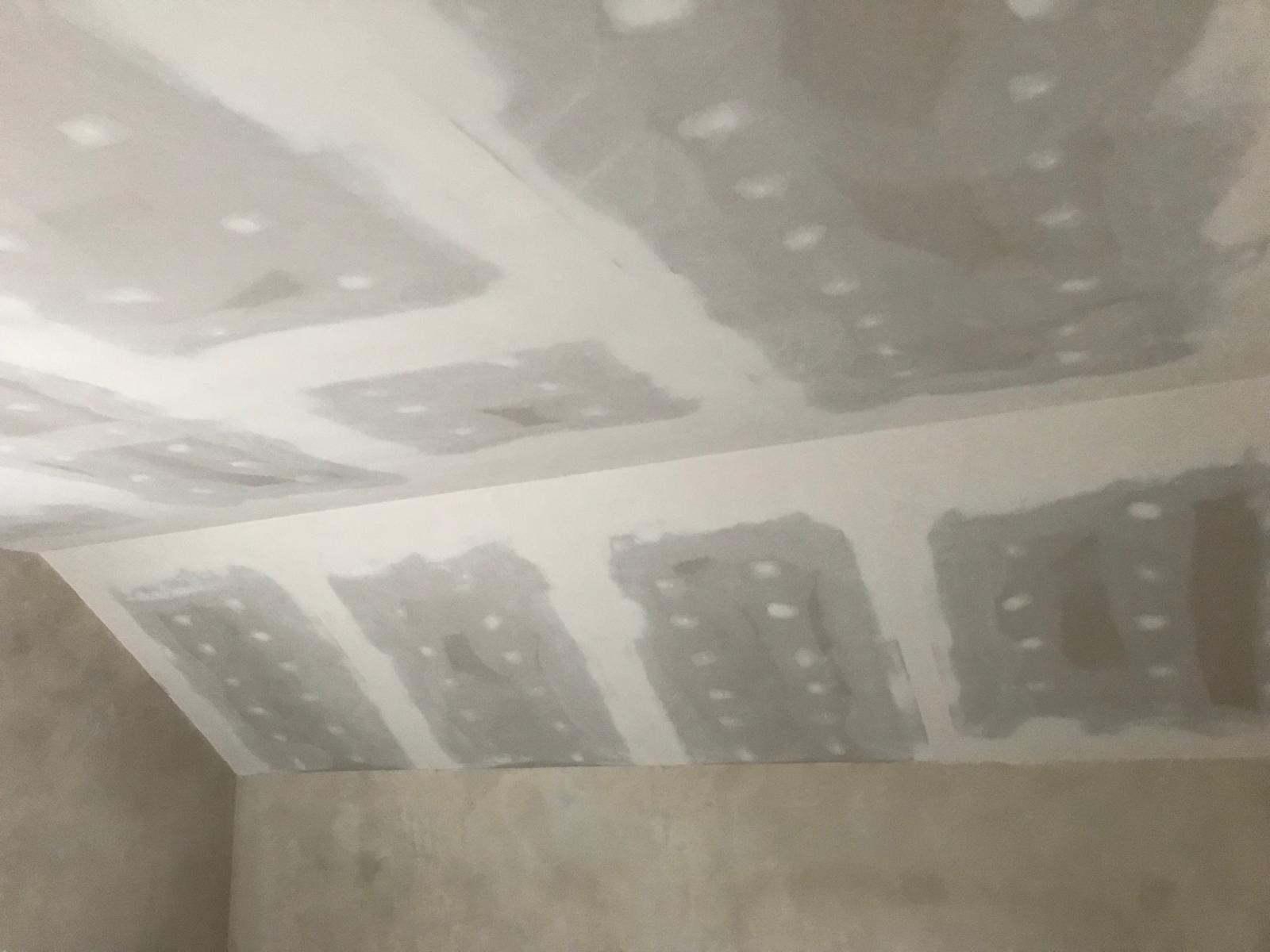 Sufit poddasza w trakcie szpachlowania, widoczne łączenia płyt gipsowo-kartonowych z nałożoną masą szpachlową, surowa ściana w tle.