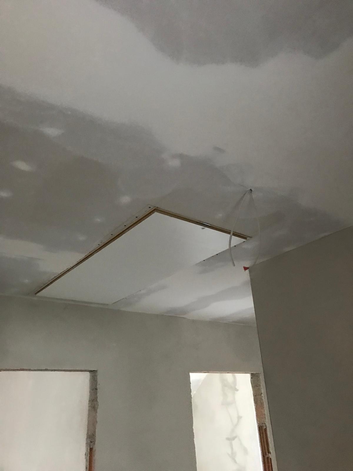 Niedokończony sufit podwieszany z widocznymi przewodami elektrycznymi w pomieszczeniu w trakcie prac wykończeniowych, ściany przygotowane do malowania.