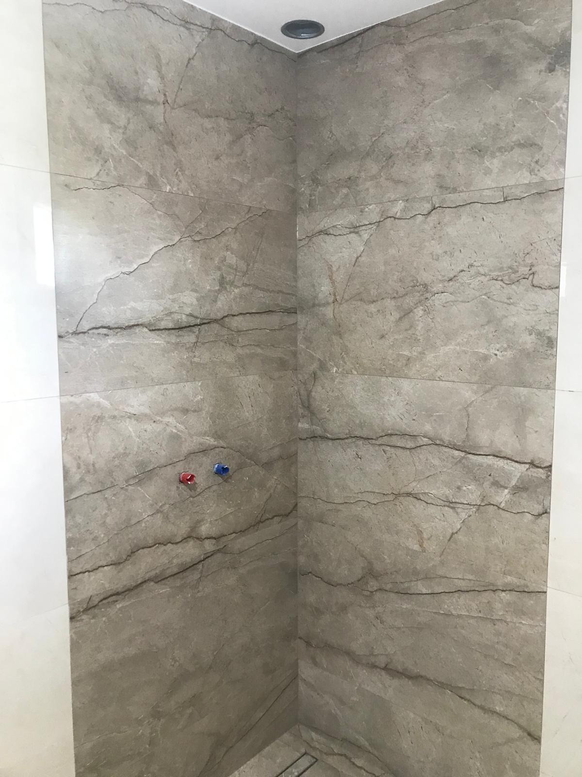 Ściany kabiny prysznicowej wyłożone płytkami imitującymi marmur, widoczne przyłącza wody z zaślepkami w kolorze czerwonym i niebieskim.