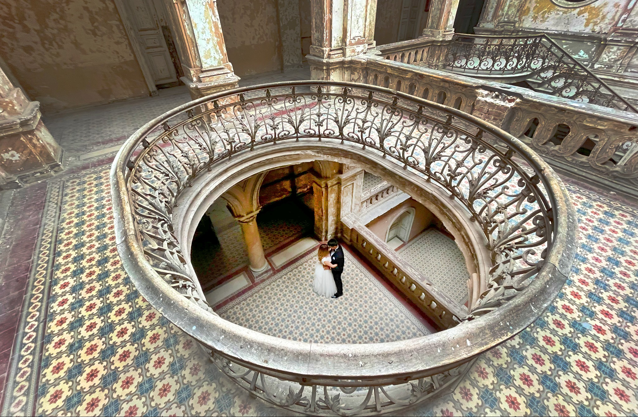 Para młoda obejmująca się na zabytkowej klatce schodowej z kutą balustradą i wzorzystą posadzką w opuszczonym budynku.