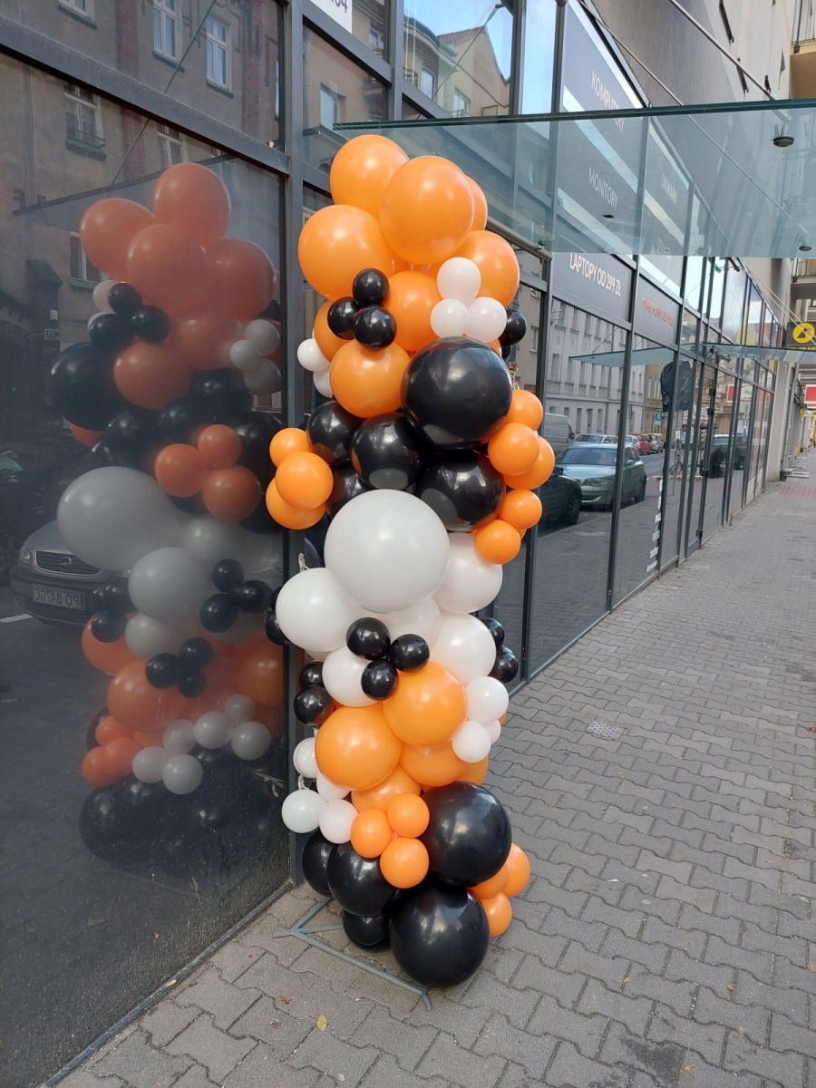 Dekoracja wejścia do budynku z balonów w kolorach pomarańczowym, białym i czarnym, z odbiciem w szybie
