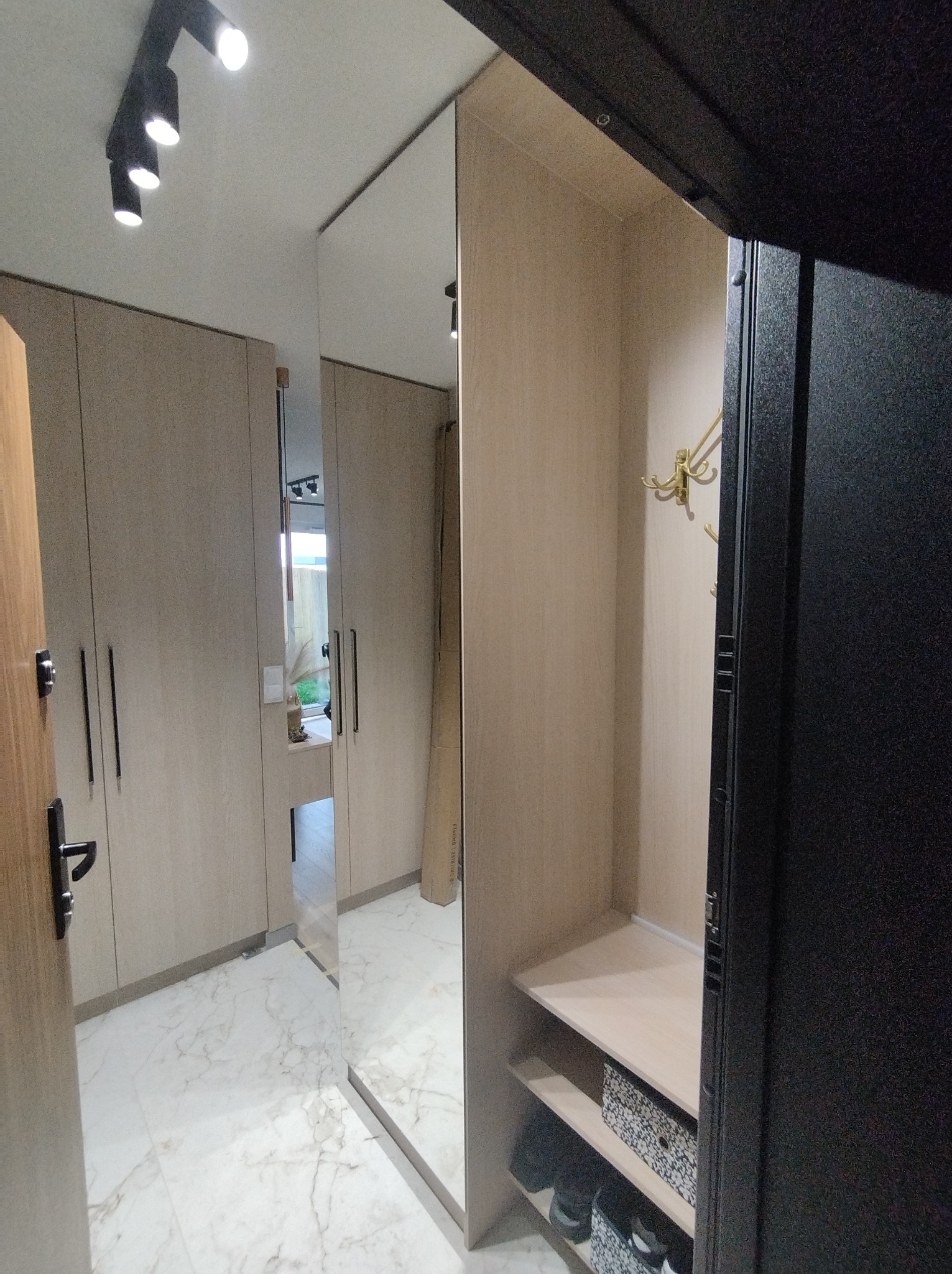 Wnętrze przedpokoju z szafą wnękową z lustrzanymi drzwiami, widoczne półki na buty i wieszaki na ubrania, oświetlenie punktowe na suficie.