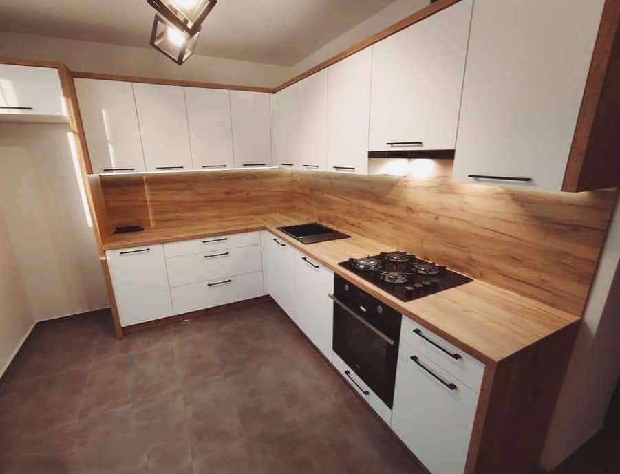 Biała kuchnia z drewnianymi akcentami, czarnymi uchwytami, płyta gazowa i piekarnik w zabudowie, oświetlenie sufitowe.