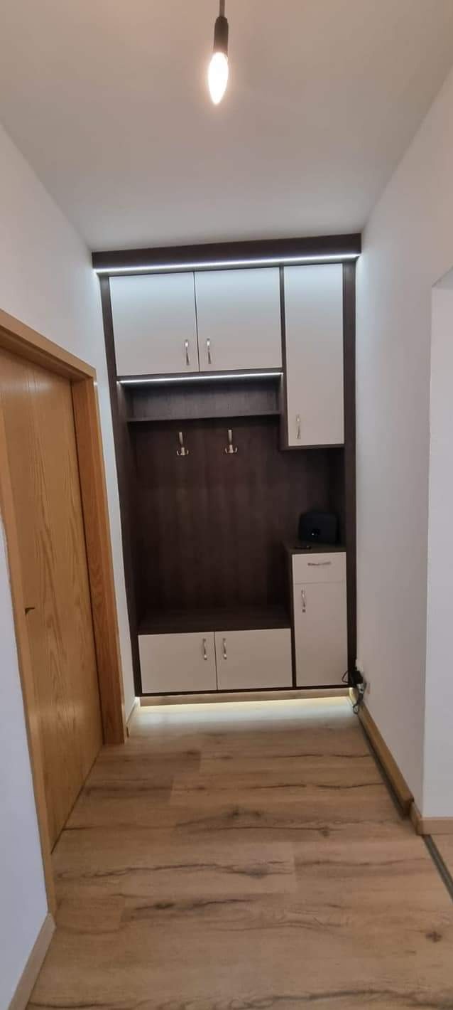 Zabudowa przedpokoju z szafkami górnymi i dolnymi w kolorze białym i brązowym, oświetlenie LED pod szafkami, drewniana podłoga.