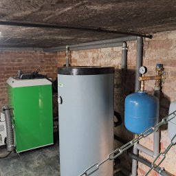 Idea Trader - Kotłownia z piecem na pellet, zbiornikiem buforowym i instalacją hydrauliczną w piwnicy z ceglanym murem i betonowym sufitem.