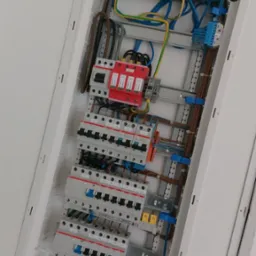 Otwarta skrzynka elektryczna z zamontowanymi bezpiecznikami, zabezpieczeniami przepięciowymi i okablowaniem, widok z dołu.