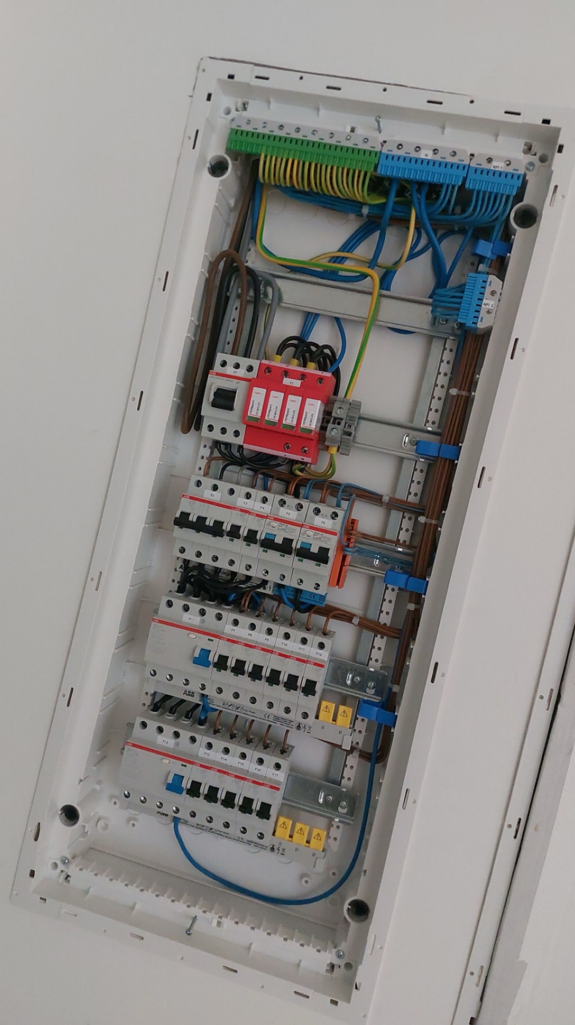 Otwarta skrzynka elektryczna z zamontowanymi bezpiecznikami, zabezpieczeniami przepięciowymi i okablowaniem, widok z dołu.