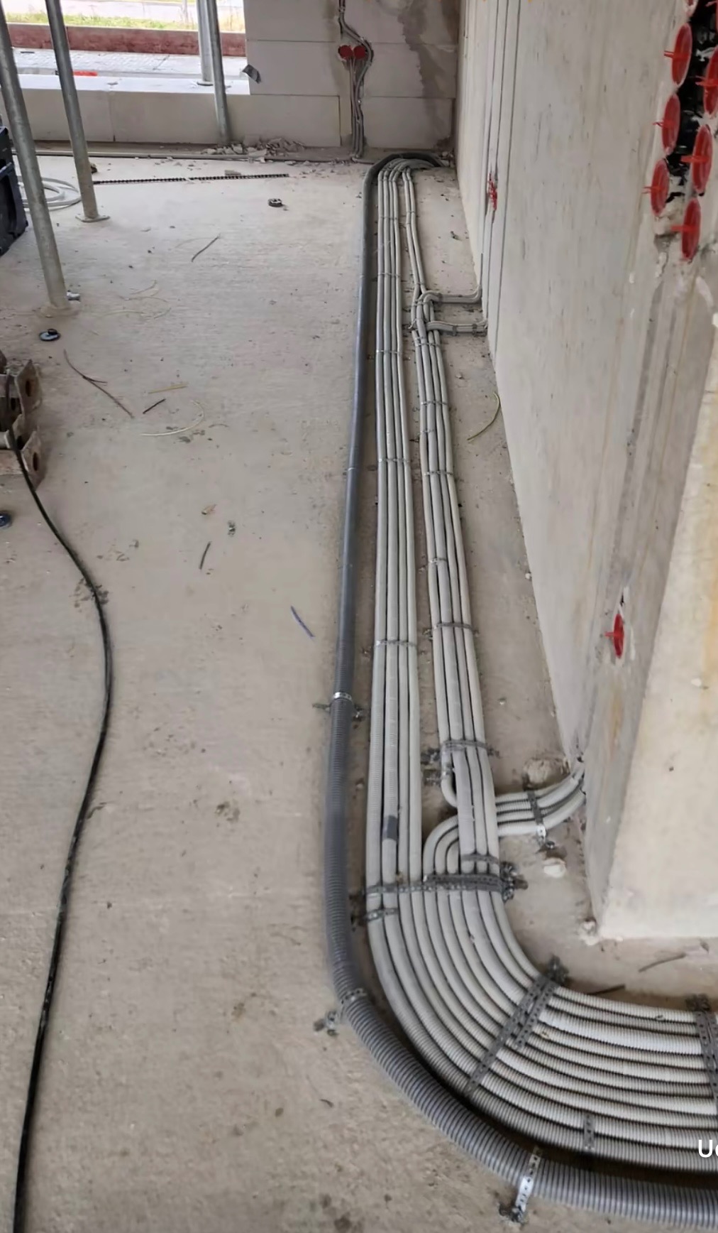 Rzędy szarych, karbowanych rur ochronnych na kable elektryczne zamocowane do surowej ściany budynku w trakcie budowy.