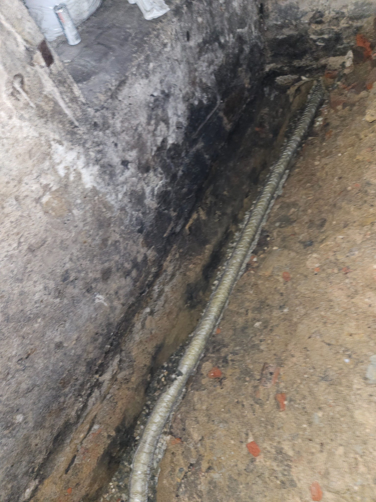 Rura w wykopie, prawdopodobnie podczas prac ziemnych związanych z podłączeniem do sieci wodno-kanalizacyjnej. Widoczne ślady ziemi i gruzu.