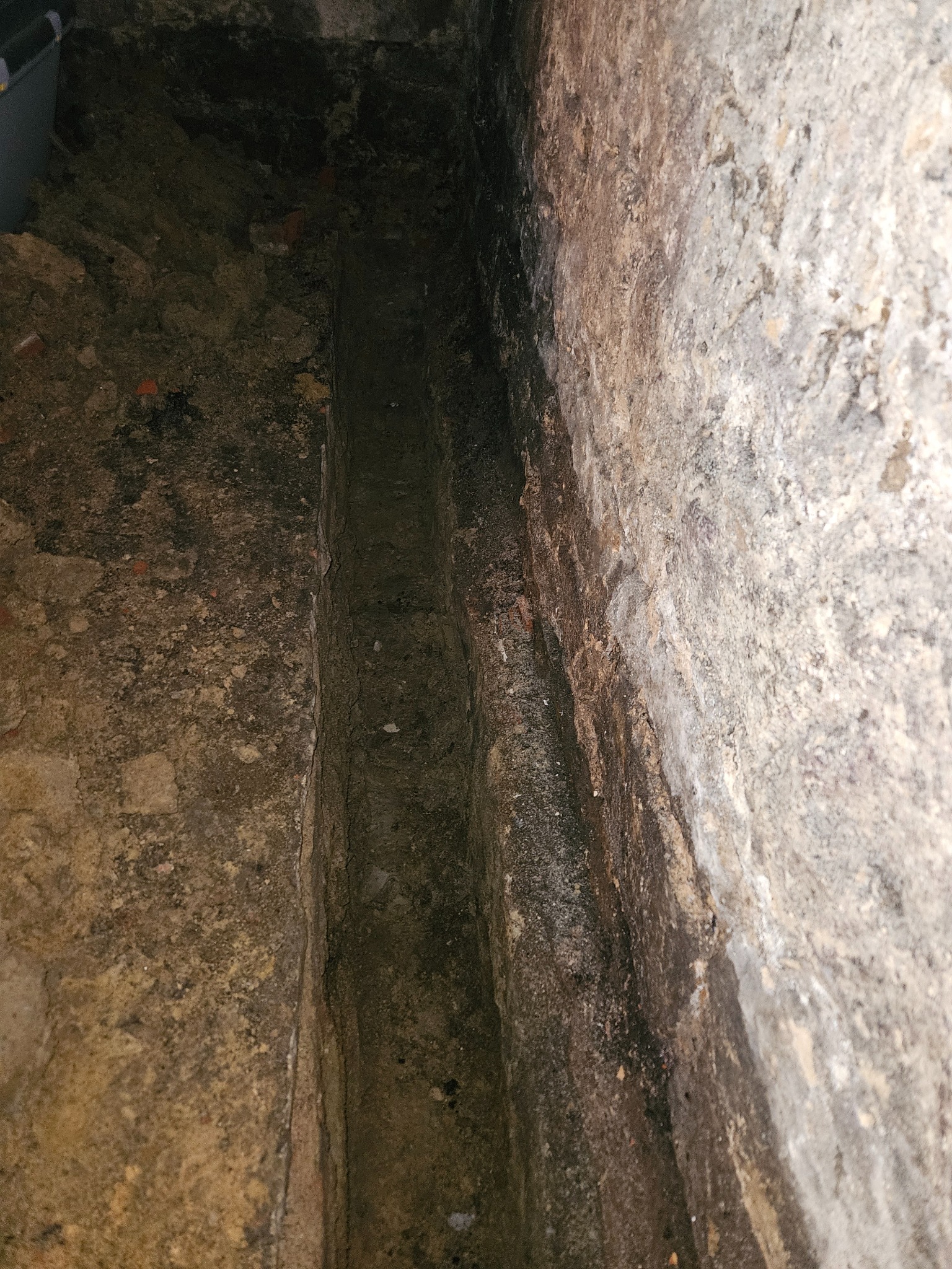 Wykop w ziemi między ścianami z cegły i betonu, prawdopodobnie pod instalację wodno-kanalizacyjną.