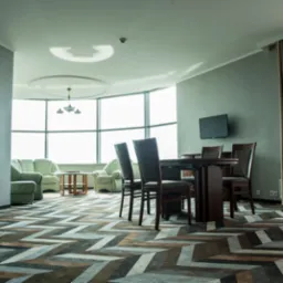 Wnętrze pokoju z wzorzystą podłogą w zygzaki, ciemnobrązowy stół i krzesła, skórzane sofy w tle, panoramiczne okno z widokiem.