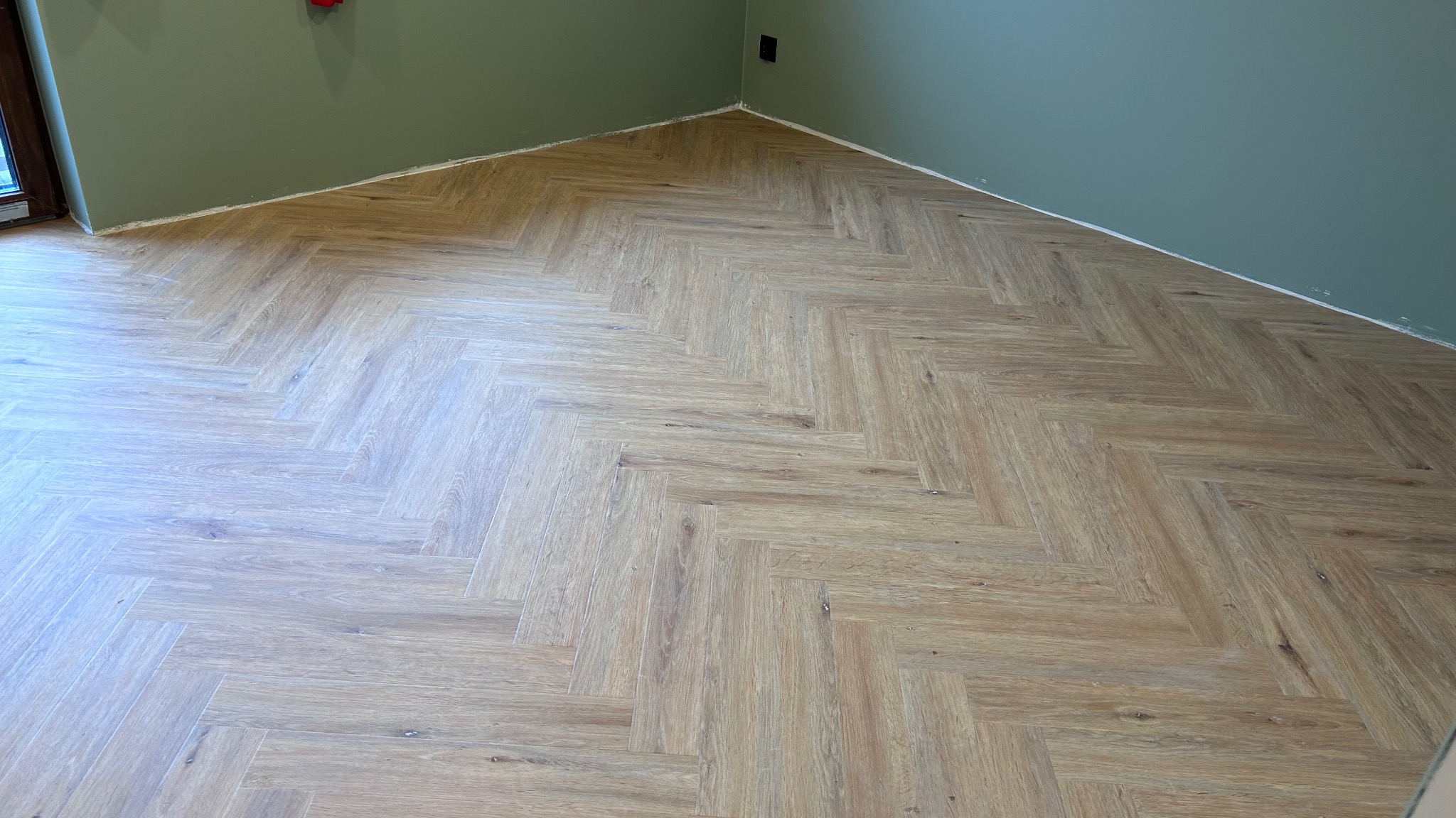 Ułożona w jodełkę podłoga z paneli imitujących drewno, widoczne ściany w odcieniach zieleni, listwy przypodłogowe jeszcze nie zamontowane.