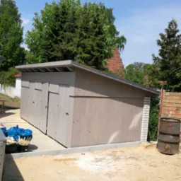 Nowo wybudowany drewniany garaż z czterema drzwiami, widoczne materiały budowlane i przygotowany teren.