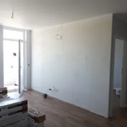 Pokój w trakcie wykańczania: świeżo położone panele podłogowe, ściany po wstępnym wyrównaniu, widoczne puszki paneli Stegu Timber, wystające przewody elektryczne z sufitu, otwarte drzwi balkonowe...