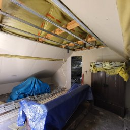 KB EFEKT Bartek Kartuszyński - Poddasze w trakcie adaptacji: widoczne metalowe profile sufitowe, częściowo zamontowana płyta gipsowa, izolacja i zabezpieczone meble. Prace wykończeniowe w toku.