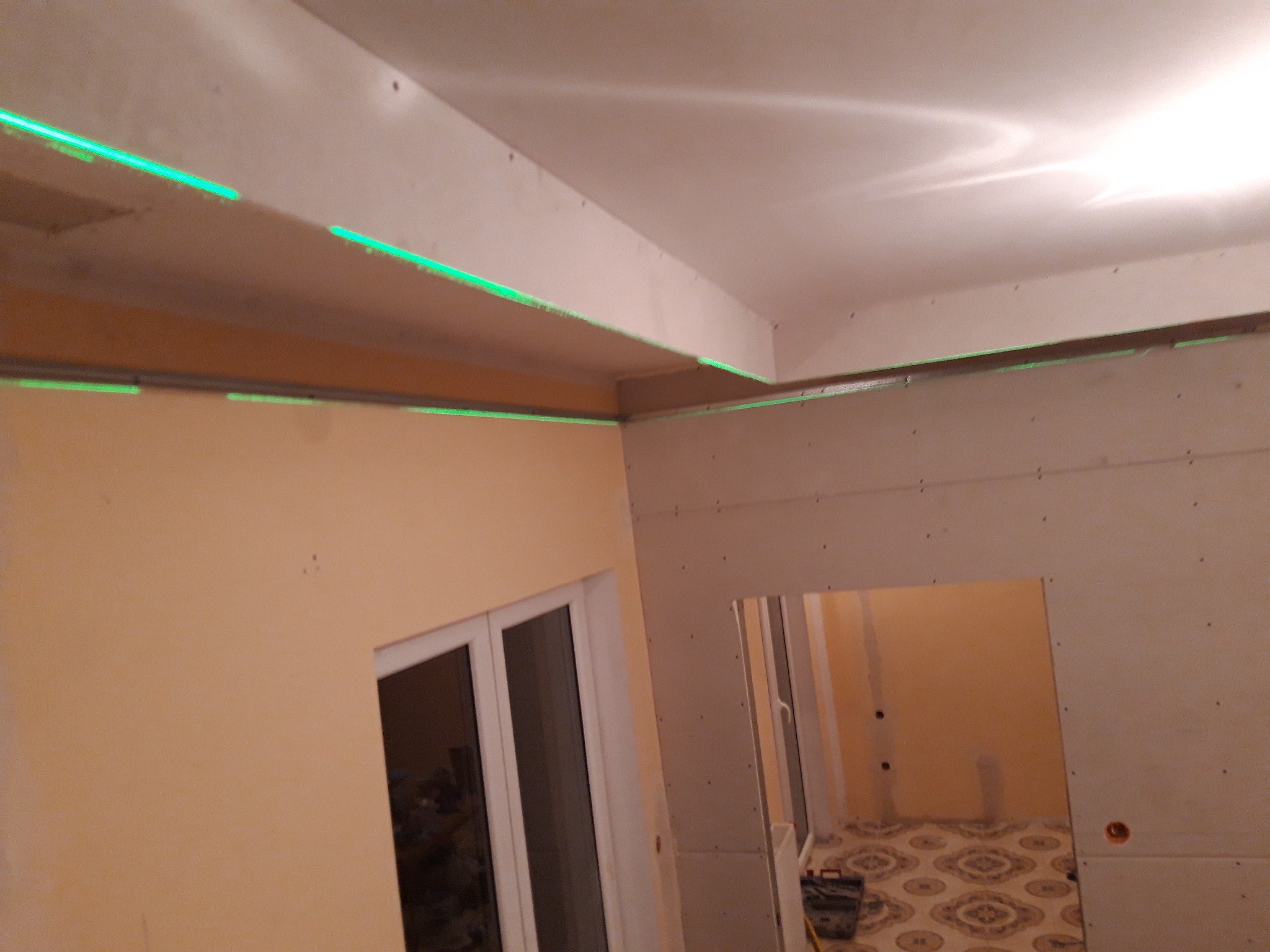 Montaż płyt kartonowo-gipsowych na ścianie i suficie, widoczne zielone linie lasera wyznaczające poziom, otwór drzwiowy w tle.