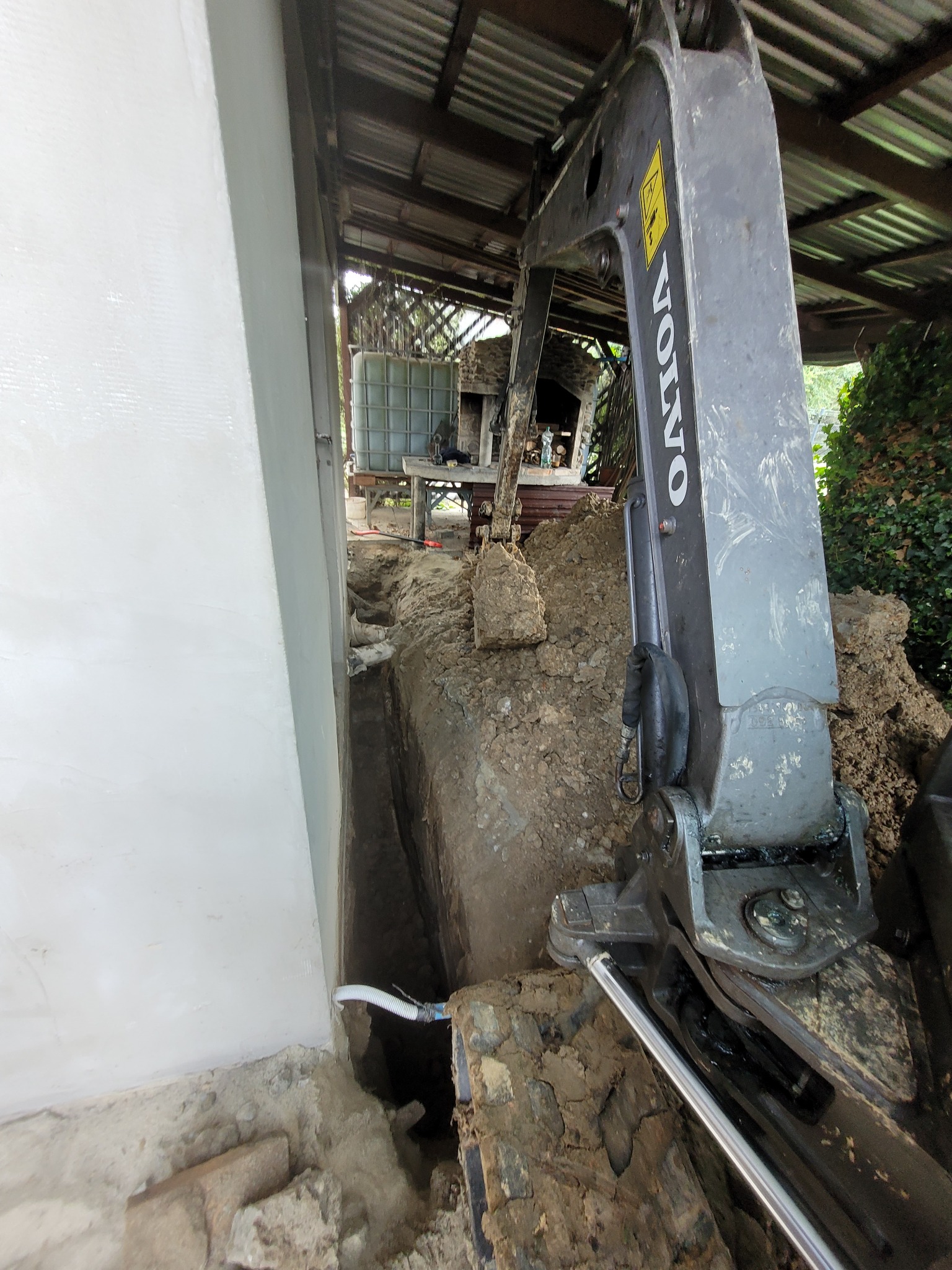 Fundament budynku po świeżej izolacji, obok wykopany wąski rów, w tle widoczny fragment koparki Volvo.