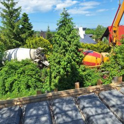 NORBUD - Widok z góry na przygotowany szalunek stropu Teriva z widocznymi betonowymi pustakami i zbrojeniem, w tle dwa betoniarki ukryte w zieleni i żuraw budowlany.