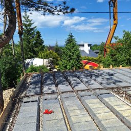 NORBUD - Wiązanie zbrojenia na stropie Teriva z pustaków szalunkowych, widoczna pompa do betonu i betonomieszarka w tle, na pustakach leżą czerwone rękawice robocze.