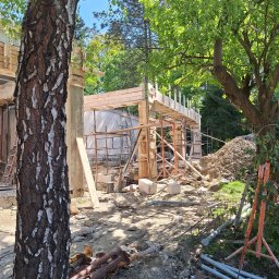 NORBUD - Budowa domu w trakcie realizacji, widoczne drewniane szalunki, rusztowania i stos ziemi, z przodu brzoza.