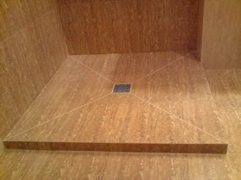 Wykończony brodzik prysznicowy z beżowych płytek imitujących trawertyn, z centralnie umieszczonym odpływem i delikatnymi fugami.