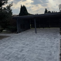 Oleksandr Chyplyk - Szara kostka brukowa ułożona na podjeździe z zadaszeniem, widok z góry, pochmurne niebo w tle. Nowoczesny wzór kostki, równa powierzchnia, estetyczne wykończenie obrzeży.