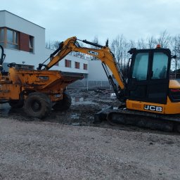 MI-TRANS Mirosław Mitrowski - Żółta minikoparka JCB i wywrotka Thwaites w błotnistym terenie budowy, na tle nowoczesnego budynku z płaskim dachem i drzew bez liści.