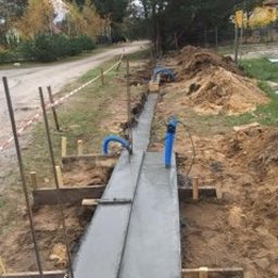 Olomk Waldemar Schulz - Wąski fundament betonowy w drewnianym szalunku, przygotowany pod budowę ogrodzenia, widoczne rury instalacyjne wystające z ziemi.