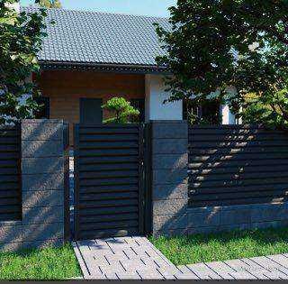 Nowoczesne ogrodzenie z poziomych desek kompozytowych w kolorze antracytowym, osadzone na słupkach z szarego betonu architektonicznego, z furtką z tego samego materiału. Widoczne wejście do domu...