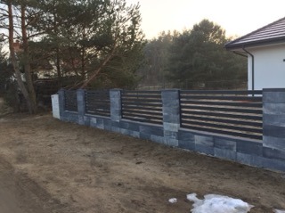 Nowoczesne ogrodzenie poziome z elementami betonowymi w Jeżewie, z widoczną strukturą kamienia na słupkach i podmurówce.