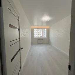 Wnętrze pokoju po remoncie: jasne panele podłogowe, wzorzyste, jasne ściany, białe drzwi z czarnymi wstawkami i nowoczesna lampa sufitowa.