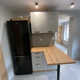 NAZBUD NAZARII HRYTSYNA - Nowoczesna kuchnia z czarną lodówką, białymi szafkami i drewnianym blatem, doświetlona punktowymi lampami sufitowymi. Widok na dalszą część mieszkania.