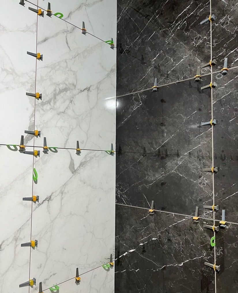 Układanie płytek marmuropodobnych w Opolu: białe i czarne płytki, system poziomowania płytek z klinami i klamrami, widoczne sznurki do wyznaczania linii.