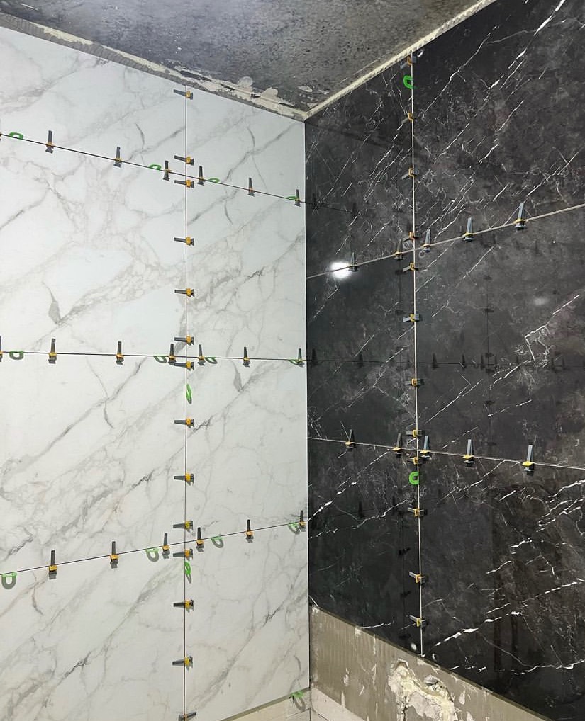Proces układania marmurowych płytek ściennych w łazience, widoczne poziomice, krzyżyki dystansowe i niezagruntowana ściana pod płytkami.