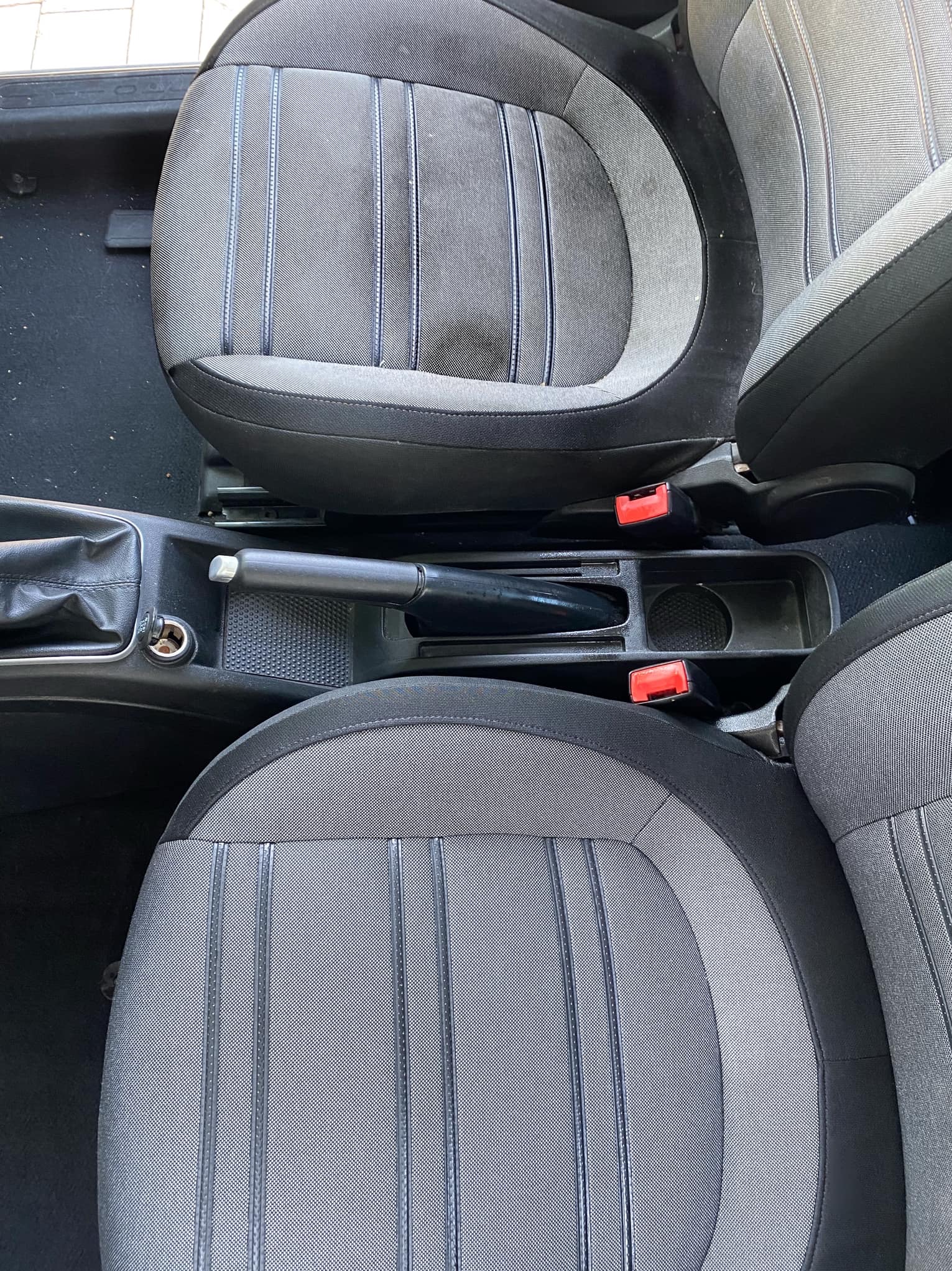 Wnętrze samochodu z szaro-czarną tapicerką foteli i podłokietnikiem; widoczne detale faktury materiału i elementy mocujące fotele.