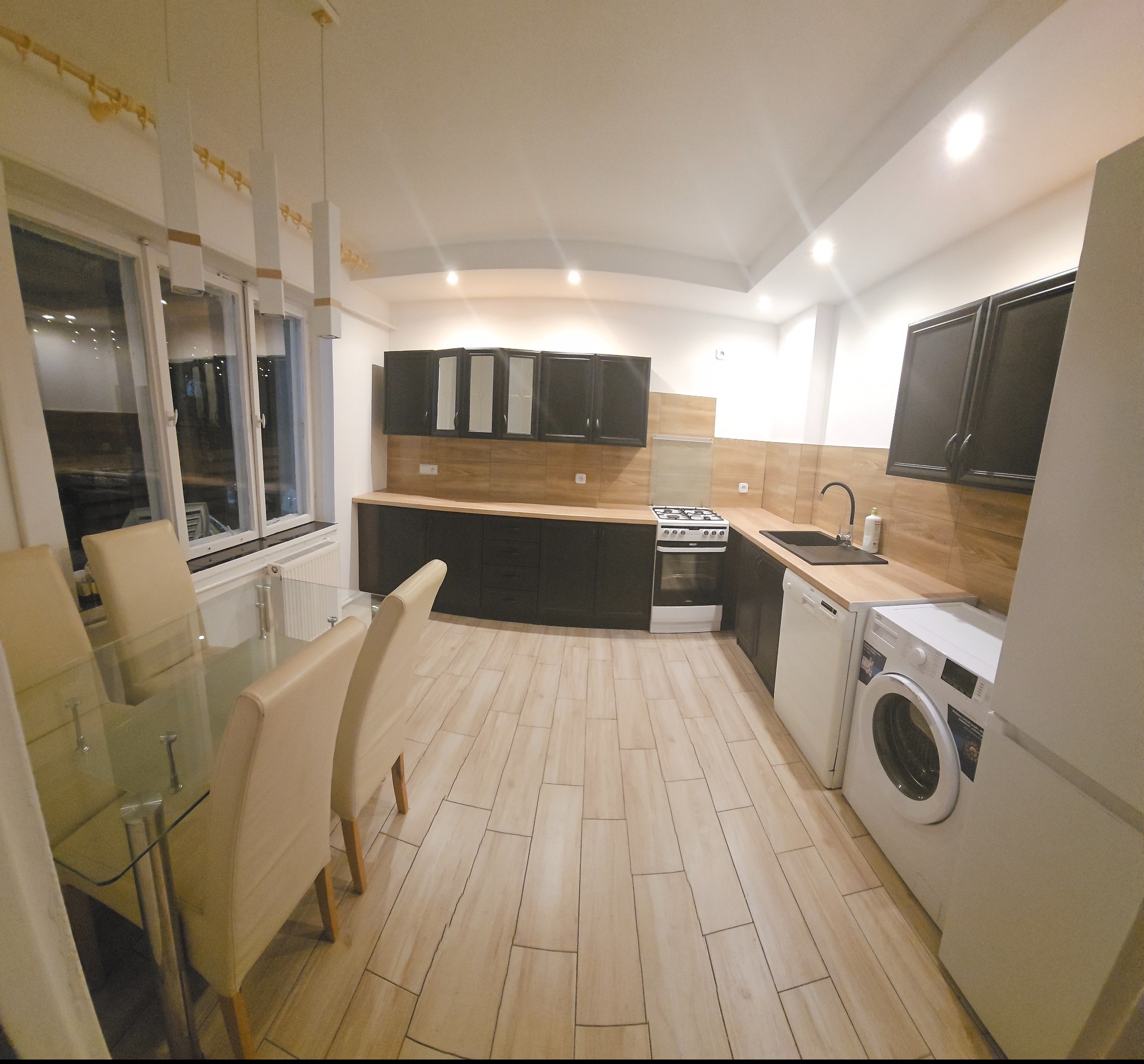 Nowoczesna kuchnia z czarnymi szafkami i drewnianym blatem w Czarnkowie. Widoczny stół z krzesłami, sprzęt AGD i jasna podłoga.