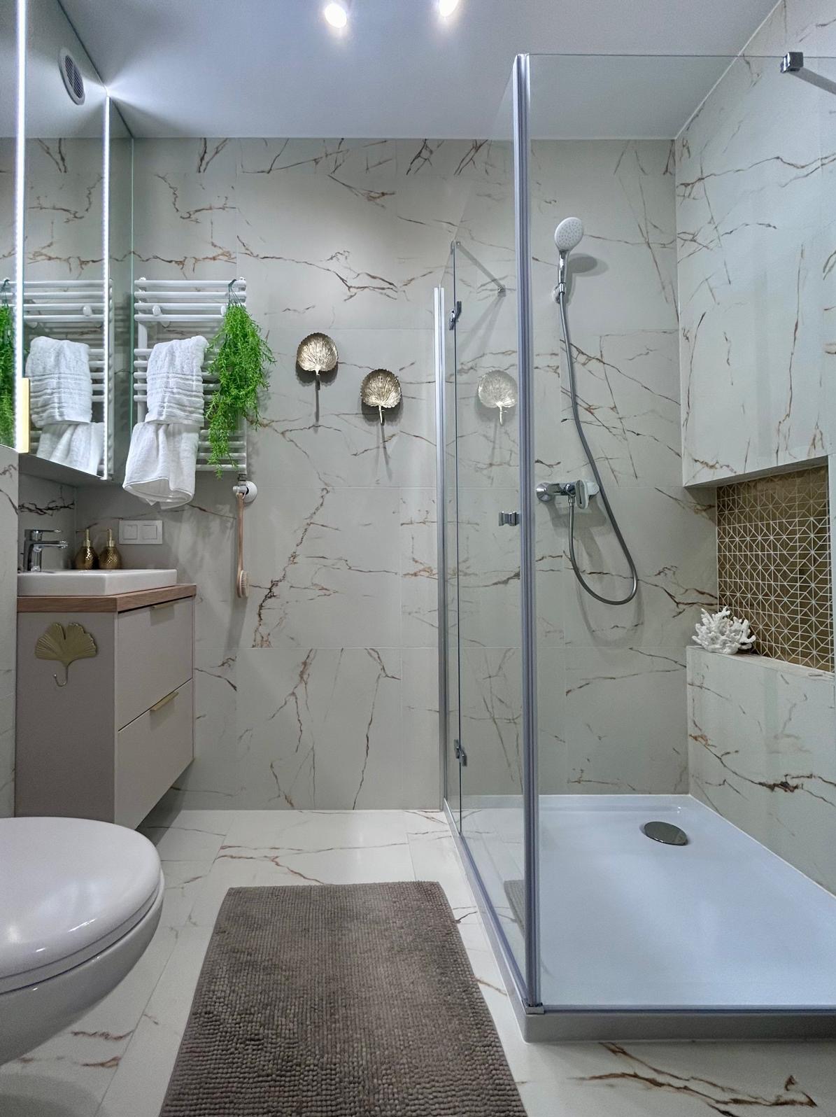 Nowoczesna łazienka z kabiną prysznicową typu walk-in, marmurowymi płytkami, umywalką z szafką zdobioną motywem liścia miłorzębu, dekoracyjnymi elementami w kształcie liści na ścianie i grzejnikiem...